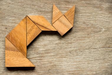 Tangram bulmaca içinde şekil ahşap arka plan üzerinde oturan kedi