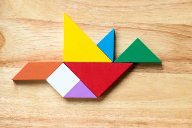 Kuş şekli ahşap arka plan üzerinde uçan renk tangram bulmacanın