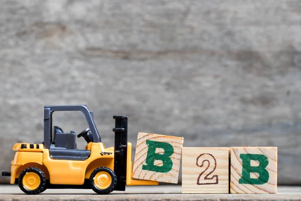 Gelbe Kunststoff-Gabelstapler halten Buchstabe b, um das Wort b2b (Business to Business) auf Holz-Hintergrund zu vervollständigen — Stockfoto