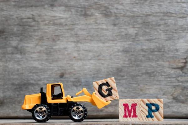 Bulldozer plástico amarelo segurar letra G para completar a palavra GMP (abreviatura de boas práticas de fabricação) sobre fundo de madeira — Fotografia de Stock