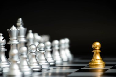 Satranç oyununda altın piyon siyah zemin üzerinde diğer gümüş takım ile birlikte (Şirket stratejisi, iş zaferi veya karar kavramı)
