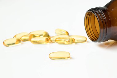 Beyaz arka plan üzerinde kehribar cam şişe ile şeffaf sarı yumuşak jelatin kapsül