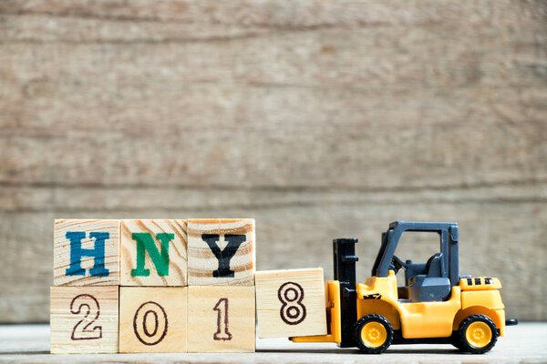 Игрушечная желтая фортепиано держит букву 8 в конце слова HNY 2018 (аббревиатура Happy new year) на деревянном фоне
