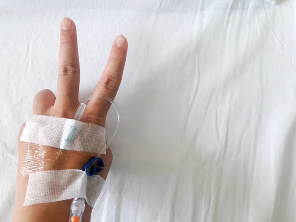 Patiënt hand met V-teken en de buis van normale saline infusion op witte doek achtergrond (overwinning van de ziekte) — Stockfoto