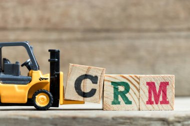 Oyuncak sarı forklift tutun kelime Crm (müşteri ilişkileri yönetimi kısaltması) ahşap arka plan üzerinde tamamlamak için mektup blok