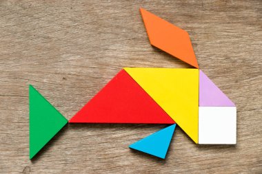 Ahşap arka plan üzerinde balık veya sazan şekli Yüzme içinde renkli tangram bulmacanın