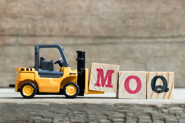 Speelgoed gele vorkheftruck houden brief blok M om te voltooien woord Moq (afkorting van Minimum Order Quantity) op houten achtergrond — Stockfoto