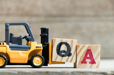 Oyuncak sarı forklift ahşap arka plan üzerinde kelime Qa (kalite güvence kısaltma veya Sıkça Sorulan Sorular) tamamlamak için mektup blok Q tutun