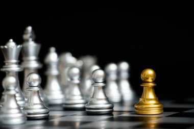 Satranç oyununda altın piyon siyah zemin üzerinde diğer gümüş takım ile birlikte (Şirket stratejisi, iş zaferi veya karar kavramı)