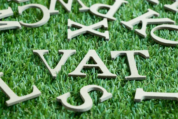Wood letter in word VAT (Abberviation of Value added tax) on artificial green grass wit English alphabet background