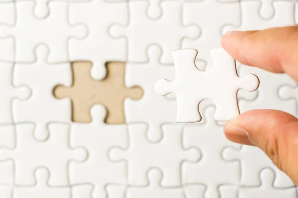 Closed up background of white plain jigsaw with hand that hold missing piece to match or fulfill — Stock Photo, Image