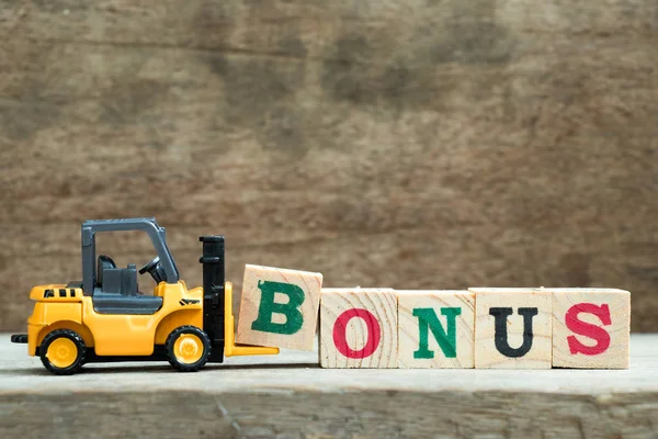 Carretilla elevadora de juguete amarillo mantenga el bloque de letras B para completar el bono de palabra en el fondo de madera —  Fotos de Stock