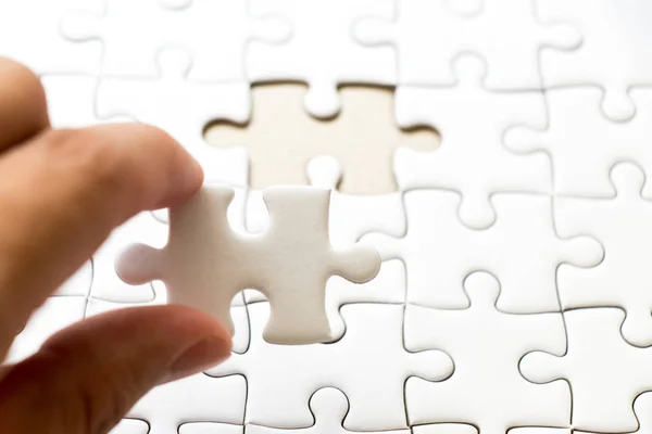 Closed up background of white plain jigsaw with hand that hold missing piece to match or fulfill — Stock Photo, Image