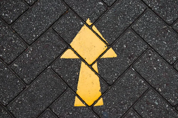 Yellow arrow paint on black brick concrete background