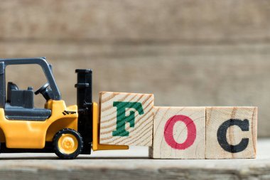 Oyuncak sarı forklift tutun kelime Foc (kısaltma, ücretsiz) tamamlamak için mektup blok F ahşap arka plan üzerinde 