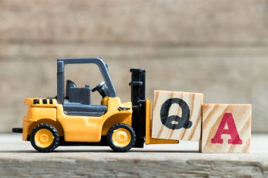 Oyuncak sarı forklift ahşap arka plan üzerinde kelime Qa (kalite güvence kısaltma veya Sıkça Sorulan Sorular) tamamlamak için mektup blok Q tutun