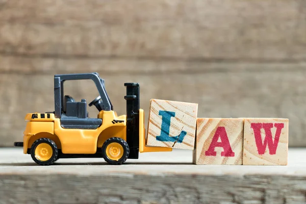 Spielzeug gelb Gabelstapler halten Buchstabe Block l Wort Gesetz auf Holz Hintergrund zu vervollständigen — Stockfoto