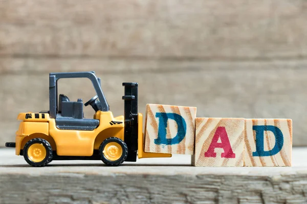 Giocattolo giallo carrello elevatore tenere lettera blocco D per completare la parola papà su sfondo di legno (concetto di giorno del padre ) — Foto Stock
