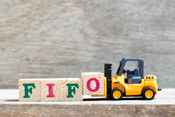 Toy forklift hold letter block FIFO (Abbreviation of first in first out) to complete word  on wood background
