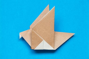 Kuş şekli mavi arka plan üzerinde uçan kahverengi origami kağıt