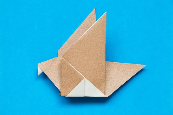 Papel de origami marrón en forma de ave voladora sobre fondo azul — Foto de Stock