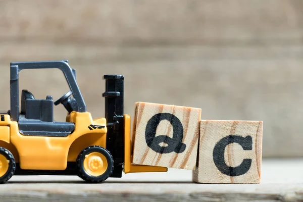 Speelgoed gele vorkheftruck houden brief blok Q te voltooien woord Qc (afkorting voor Quality Control) op houten achtergrond — Stockfoto