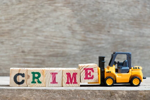 Toy forklift hold letter block E to complete word crime on wood background — Stock Photo, Image