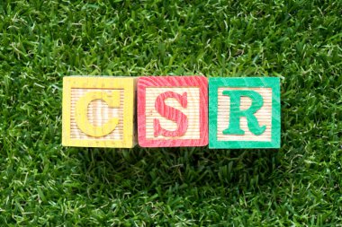Yapay yeşil çimen arka planında CSR (kurumsal sosyal sorumluluğun kısaltması) sözcüğündeki tahta bloklar