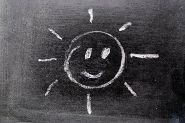 Beyaz renkli tebeşirle çizen el, karatahta arka planında ışın şeklinde.