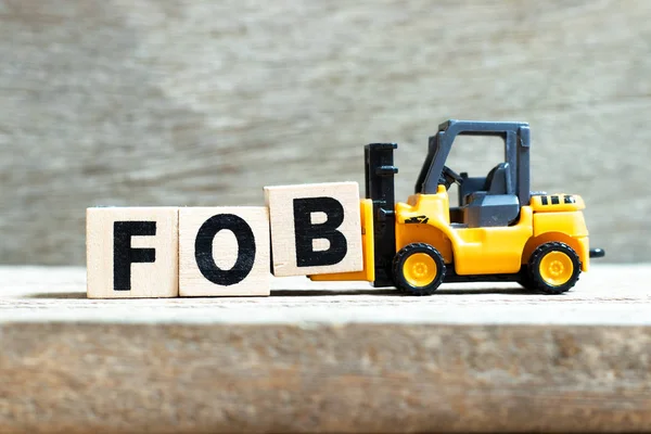 おもちゃのフォークリフトは、木製の背景に単語Fob(ボード上のフリーの略語)を完了するために文字ブロックBを保持します — ストック写真