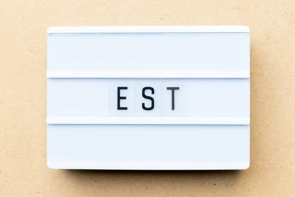 Biała skrzynka oświetleniowa ze słowem est (skrót od ustalonej, szacunkowej, wschodniej strefy czasowej, wyrażony znacznik sekwencji) na tle drewna — Zdjęcie stockowe