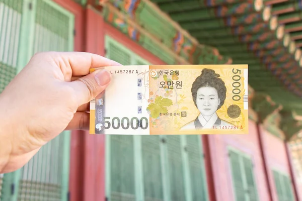 Traveller hand hold 50000 Koreański wygrał banknot na zdekoncentrowanym tle koreańskiego pałacu. — Zdjęcie stockowe