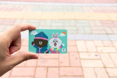 Seul, Güney Kore - 23 Ekim 2019: gezgin el ele tutuşma para kartı bulanık arka planda çizgi film karakteri. T Money, Güney Kore 'de tren, otobüs ve alışveriş için ön ödemeli bir karttır.