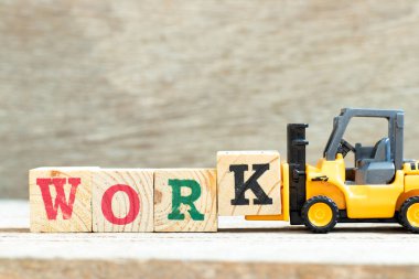 Oyuncak forklift harf bloğu k 'yi ahşap arkaplan çalışmasını tamamlamak için tutuyor