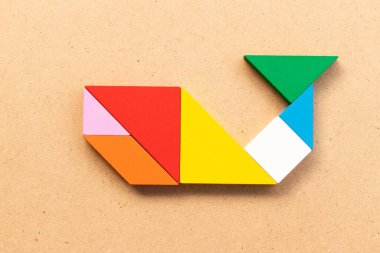 Ahşap arka planda balina, balık ya da köpekbalığı şekilli renk tangramı yapbozu