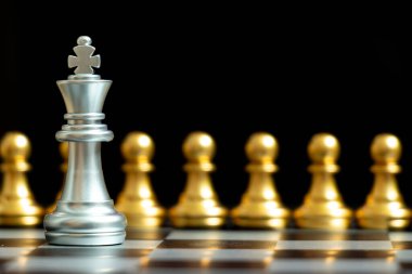 Gümüş kral satranç taşı siyah arka planda altın takım ile yüz yüze (Şirket stratejisi, iş kararı kavramı ve sorunla karşılaşma)