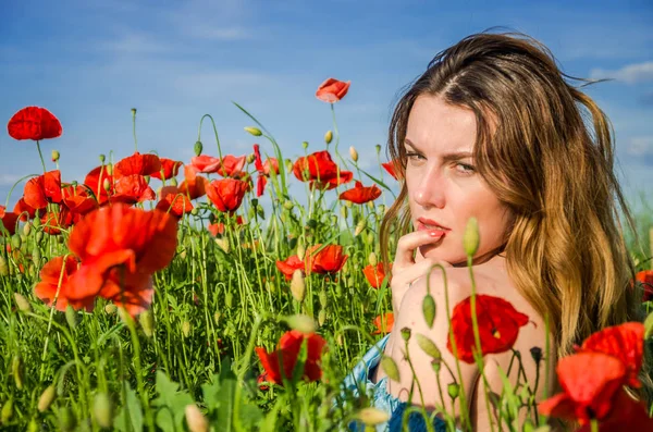 A young cheerful beautiful girl walks in a poppy meadow among red blooming poppies on a bright, hot, sunny summer day — Stock Photo, Image