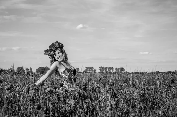 Молодая очаровательная девушка ходит по полю с цветущими маками с венком мака на голове — стоковое фото