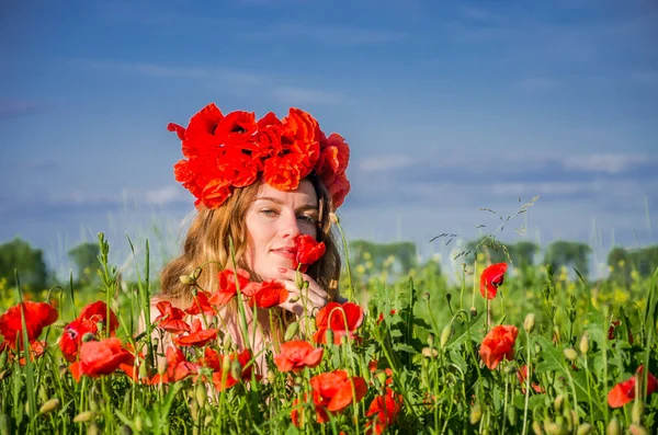 Young beautiful girl in a field of flowering poppies with a wreath of poppies on her head enjoying the aroma of a poppy flower — Stock Photo, Image