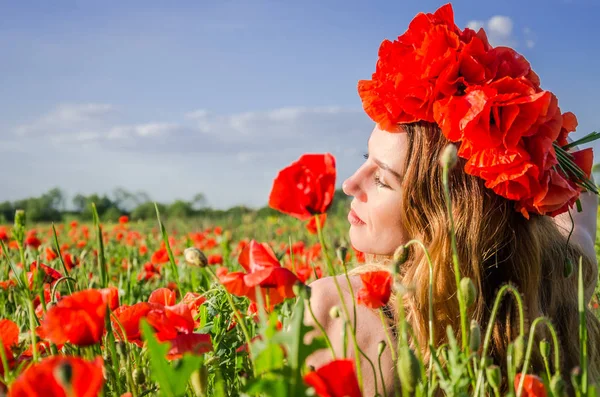 Portrait of a young beautiful girl in a poppy field with a wreath of poppies on her head on a hot summer sunny day — Stock Photo, Image