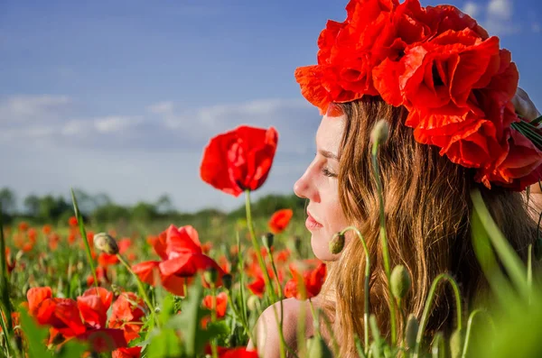 Portrait of a young beautiful girl in a poppy field with a wreath of poppies on her head on a hot summer sunny day — Stock Photo, Image