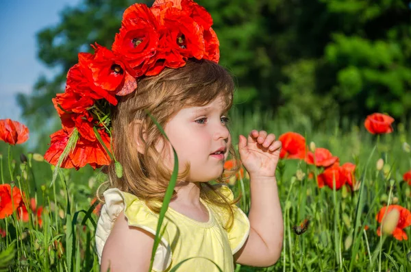 Okouzlující malá holčička v makovém poli s kyticí máků na hlavu — Stock fotografie