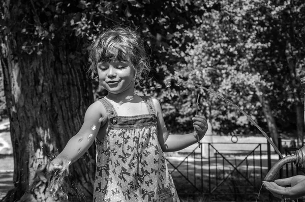 Маленькая очаровательная маленькая девочка, ребенок в платье, пьет воду из фонтана римской питьевой воды в жаркий летний день, утоляя жажду, в парке Вилла Памфили в Риме — стоковое фото