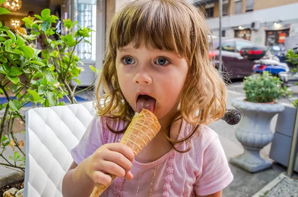 Piccola ragazza affascinante il bambino mangia e lecca le lingue del gelato in un caffè di strada a Roma, la capitale d'Italia — Foto Stock