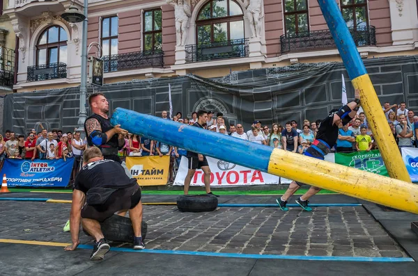 LVIV, UCRANIA - AGOSTO 2017: Un fuerte culturista atleta levanta una enorme tubería de acero pesado para el juego de hombre fuerte en frente de espectadores entusiastas — Foto de Stock
