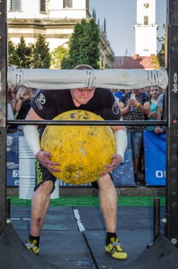 Lviv, Ukrayna - Ağustos 2017: Güçlü atlet bir vücut geliştirmeci Strongmen oyunlarda büyük bir ağır taş sarı topun asansörleri