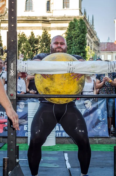 LVIV, UCRANIA - AGOSTO 2017: Un atleta fuerte un culturista levanta una enorme bola amarilla de piedra pesada en los juegos de Strongmen — Foto de Stock