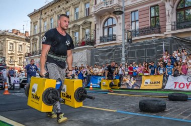 Lviv, Ukrayna - Ağustos 2017: Güçlü atlet bir vücut geliştirmeci egzersiz ağır demir bavul bir çiftçinin yürüyüş, coşkulu seyirci önünde strongmen oyun taşır