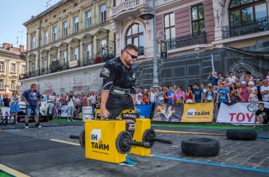 Lviv, Ukrayna - Ağustos 2017: Güçlü atlet bir vücut geliştirmeci egzersiz ağır demir bavul bir çiftçinin yürüyüş, coşkulu seyirci önünde strongmen oyun taşır