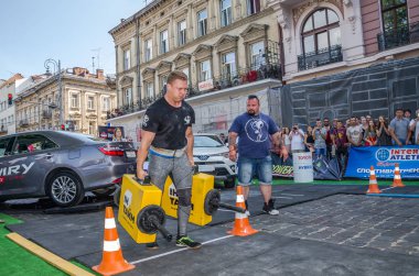 Lviv, Ukrayna - Ağustos 2017: Güçlü atlet bir vücut geliştirmeci egzersiz ağır demir bavul bir çiftçinin yürüyüş, coşkulu seyirci önünde strongmen oyun taşır